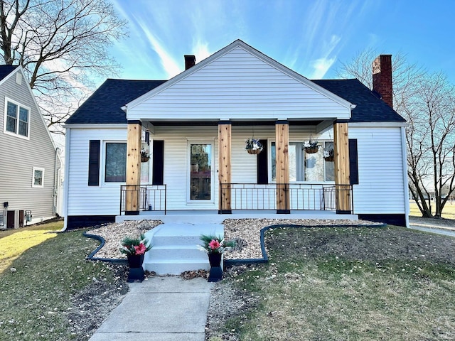 bungalow-style home featuring covered porch, a chimney, and roof with shingles