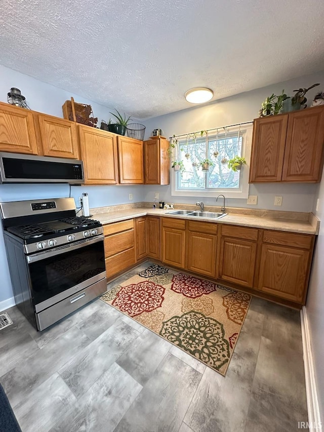 kitchen featuring a textured ceiling, a sink, light countertops, appliances with stainless steel finishes, and brown cabinetry