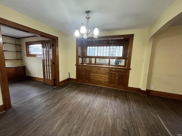 unfurnished dining area featuring arched walkways, a notable chandelier, dark wood-style floors, and baseboards