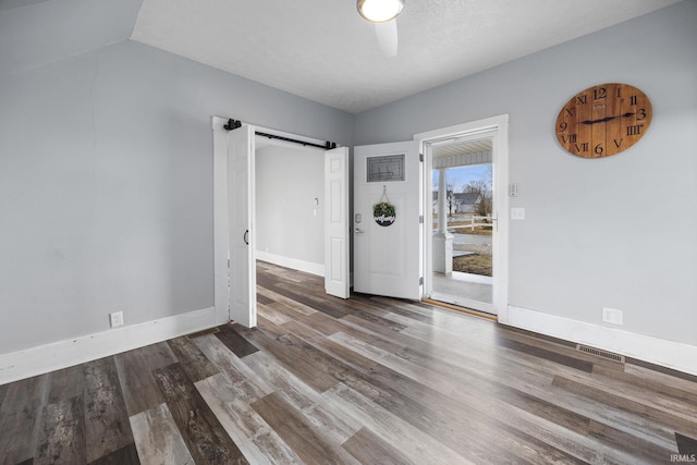 empty room featuring visible vents, a barn door, ceiling fan, wood finished floors, and baseboards