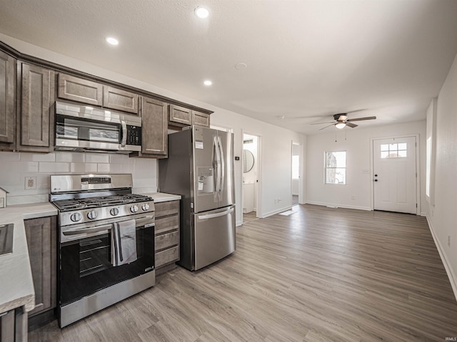 kitchen with stainless steel appliances, light countertops, light wood-style flooring, decorative backsplash, and dark brown cabinets