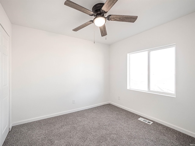 carpeted empty room featuring baseboards, visible vents, and a ceiling fan