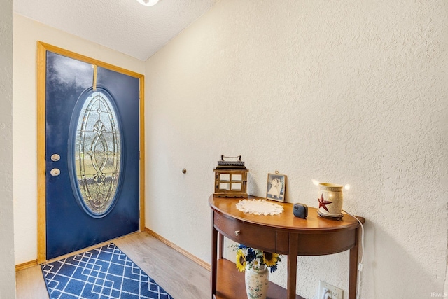 foyer with a textured wall, a textured ceiling, baseboards, and wood finished floors