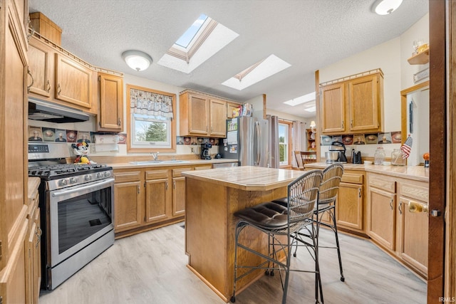 kitchen featuring a breakfast bar area, under cabinet range hood, a sink, light countertops, and appliances with stainless steel finishes