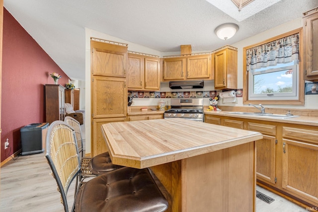 kitchen featuring a kitchen bar, a sink, a textured ceiling, under cabinet range hood, and stainless steel gas range oven