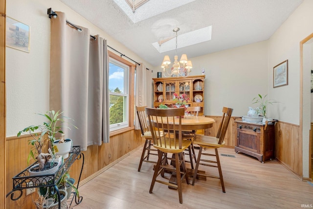 dining area with light wood-style flooring, wooden walls, a chandelier, and wainscoting