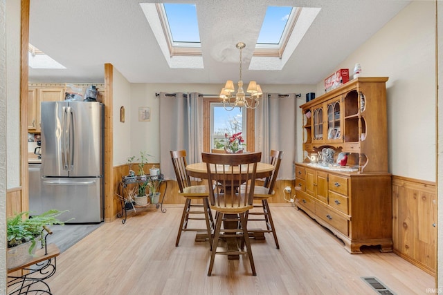 dining area featuring wood walls, visible vents, vaulted ceiling, light wood-type flooring, and wainscoting