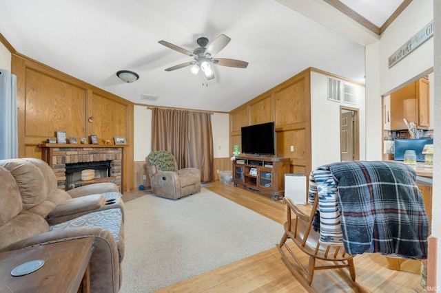 living area with wooden walls, a fireplace, visible vents, light wood-style floors, and crown molding