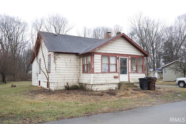 bungalow with a shingled roof, a chimney, and a sunroom