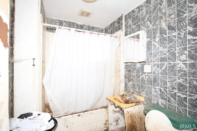 full bathroom featuring visible vents, shower / bath combo with shower curtain, and tile walls