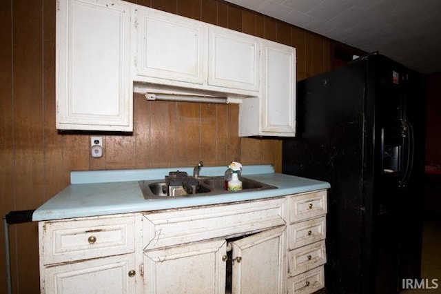 kitchen featuring wooden walls, light countertops, a sink, and black fridge with ice dispenser