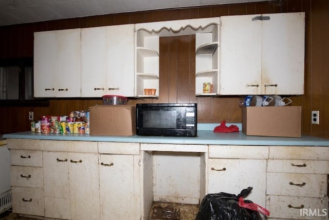 kitchen with black microwave, wood walls, white cabinetry, light countertops, and open shelves