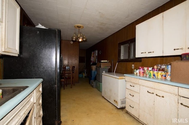 kitchen with refrigerator, light countertops, freestanding refrigerator, a sink, and wooden walls