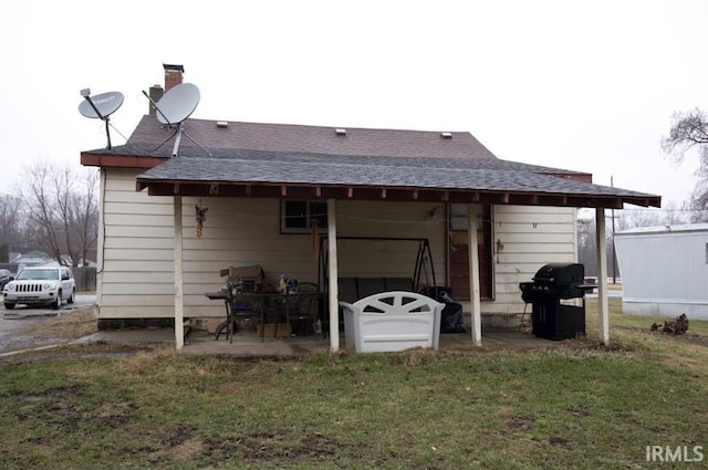 rear view of house featuring roof with shingles and a lawn