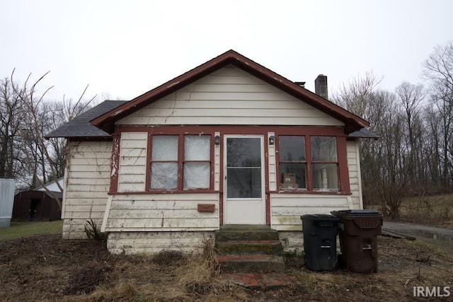 rear view of property featuring entry steps, roof with shingles, and a chimney