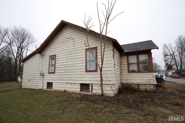 view of side of home with roof with shingles and a yard