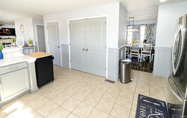 kitchen featuring light countertops, a wainscoted wall, light tile patterned flooring, and freestanding refrigerator