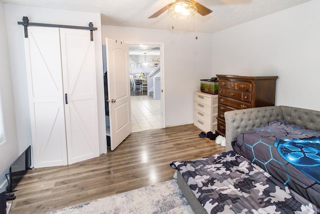 bedroom featuring ceiling fan, a barn door, and wood finished floors