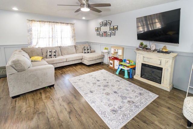 living area with a decorative wall, dark wood finished floors, a ceiling fan, wainscoting, and a glass covered fireplace