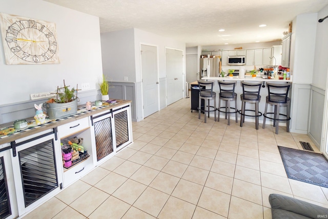 kitchen with light tile patterned floors, visible vents, a decorative wall, appliances with stainless steel finishes, and a peninsula