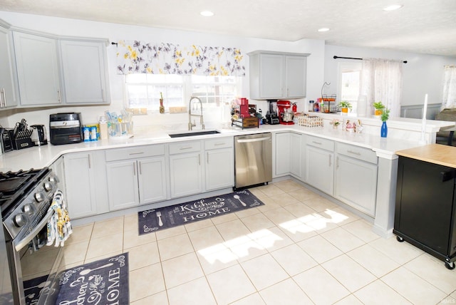 kitchen featuring appliances with stainless steel finishes, a peninsula, light countertops, a sink, and light tile patterned flooring