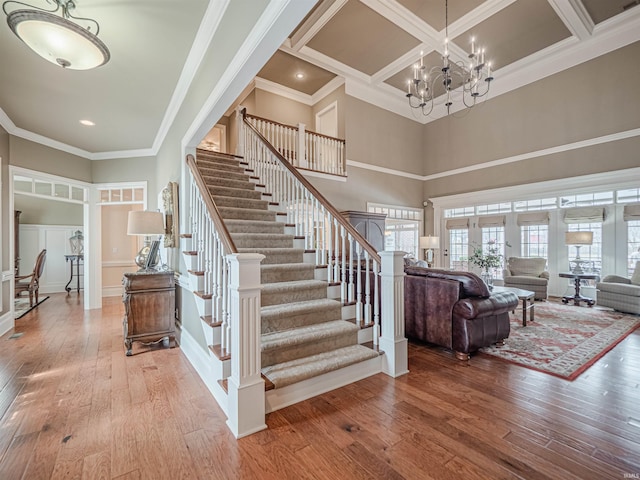 stairs with a notable chandelier, ornamental molding, coffered ceiling, and hardwood / wood-style floors