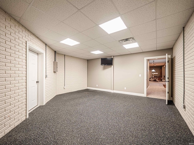 below grade area featuring a paneled ceiling, brick wall, visible vents, baseboards, and dark carpet