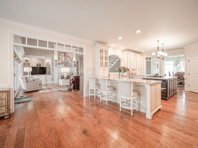 kitchen featuring a peninsula, light wood-type flooring, a kitchen bar, glass insert cabinets, and crown molding