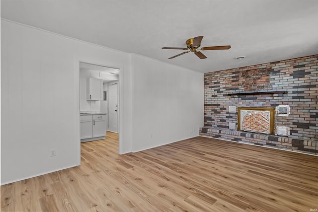 unfurnished living room with ceiling fan, brick wall, light wood-type flooring, and a brick fireplace