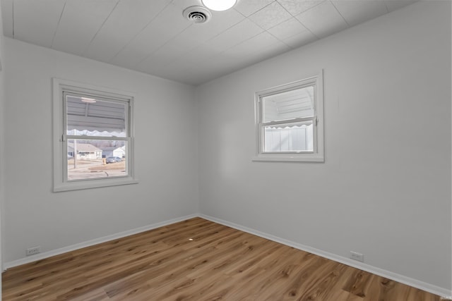 empty room featuring visible vents, wood finished floors, a wealth of natural light, and baseboards