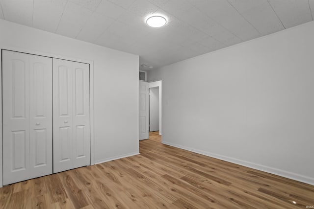 unfurnished bedroom featuring light wood finished floors, visible vents, baseboards, and a closet