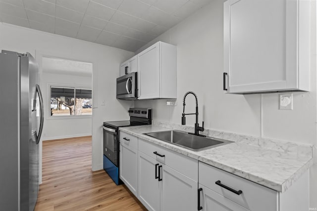 kitchen with appliances with stainless steel finishes, white cabinetry, a sink, and light wood finished floors