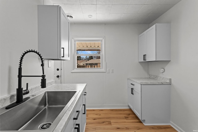 kitchen featuring light wood-type flooring, baseboards, light countertops, and a sink