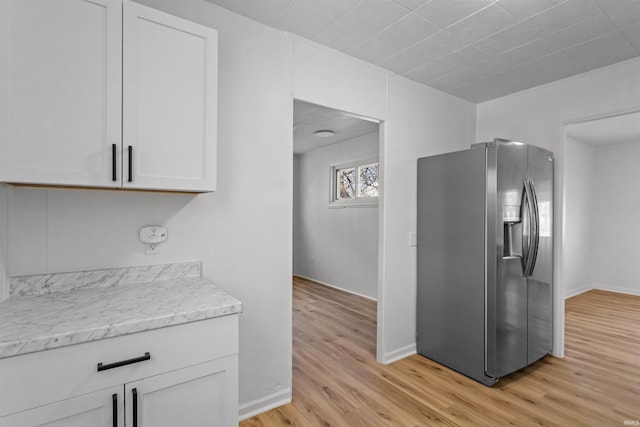 kitchen with white cabinets, stainless steel fridge, baseboards, and light wood-style flooring