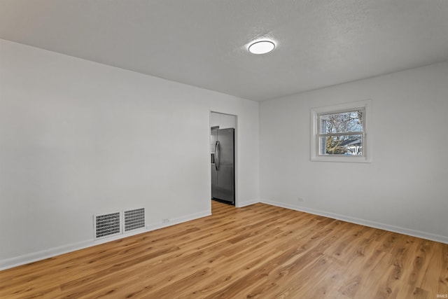 unfurnished room featuring light wood-style floors, visible vents, a textured ceiling, and baseboards