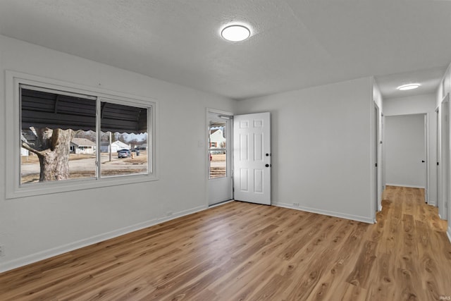 spare room featuring light wood finished floors, baseboards, and a textured ceiling