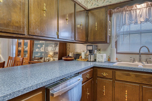 kitchen with brown cabinets, stainless steel dishwasher, backsplash, and a sink