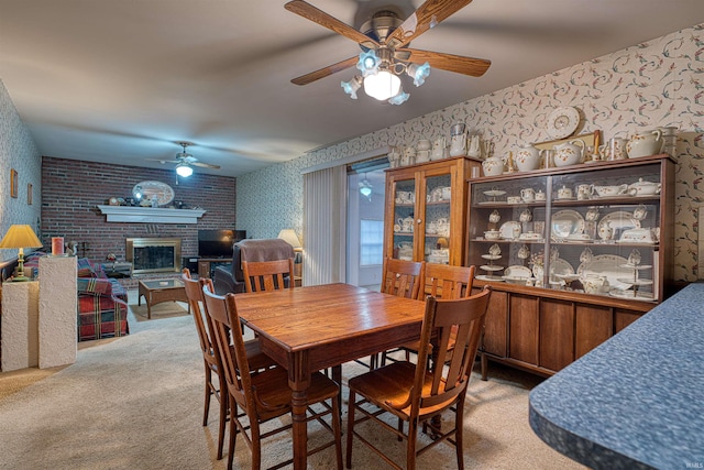 dining space with a ceiling fan, a brick fireplace, light colored carpet, and wallpapered walls