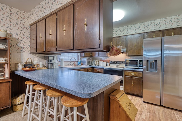 kitchen featuring wallpapered walls, light wood-style flooring, a peninsula, stainless steel appliances, and a sink