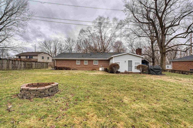 back of house with an outdoor fire pit, a chimney, fence, a yard, and brick siding