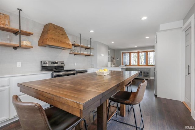 kitchen with a peninsula, stainless steel range with electric cooktop, light countertops, open shelves, and custom range hood