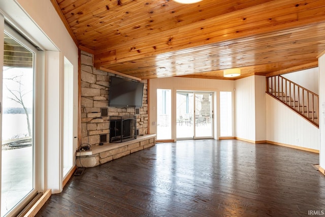 unfurnished living room featuring dark wood-style flooring, lofted ceiling, wood ceiling, a stone fireplace, and stairs