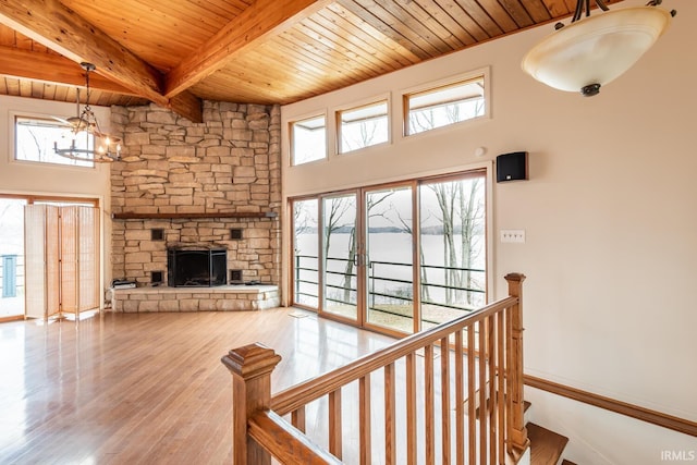 living area with a chandelier, a stone fireplace, wood finished floors, wood ceiling, and beam ceiling