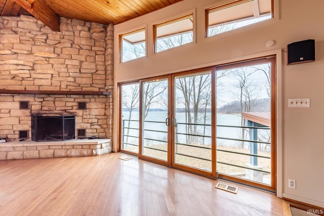 unfurnished living room featuring visible vents, wood ceiling, wood finished floors, a water view, and a fireplace