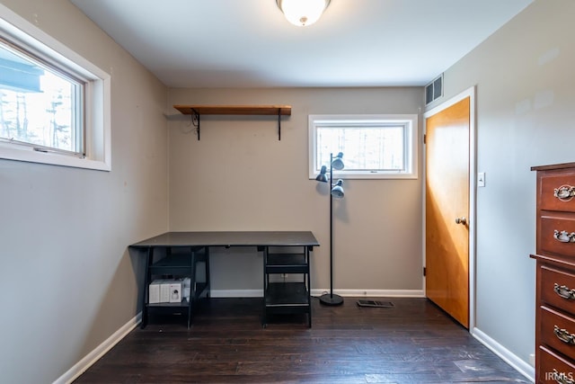 unfurnished office featuring dark wood-style floors, baseboards, visible vents, and a wealth of natural light