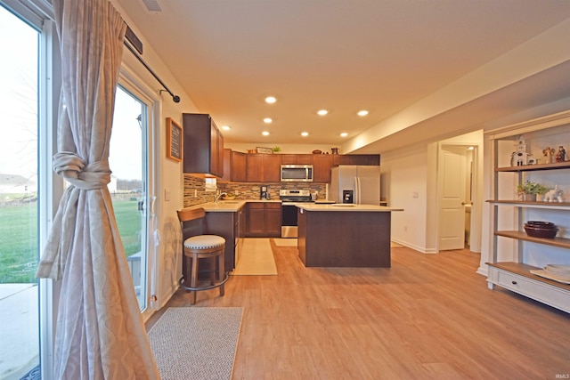 kitchen with light wood finished floors, appliances with stainless steel finishes, a center island, light countertops, and backsplash