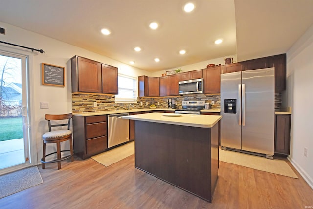 kitchen with light wood-style flooring, a center island, stainless steel appliances, light countertops, and backsplash