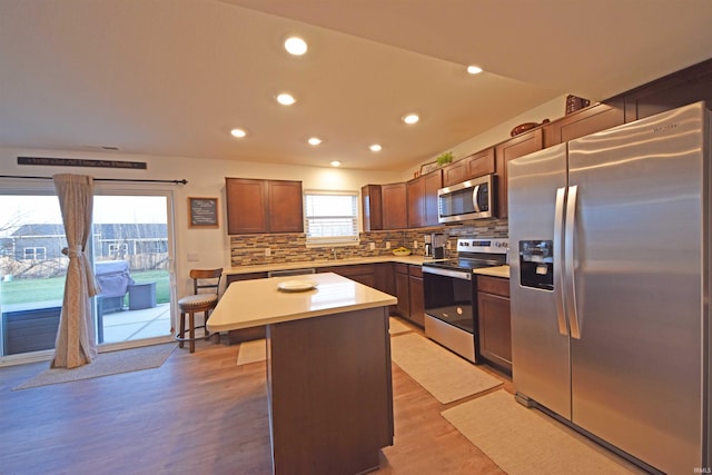 kitchen with stainless steel appliances, light countertops, a center island, light wood finished floors, and tasteful backsplash