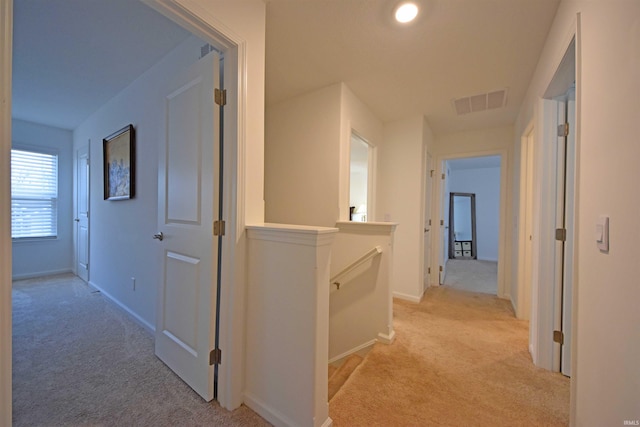 hallway with visible vents, baseboards, an upstairs landing, and light colored carpet