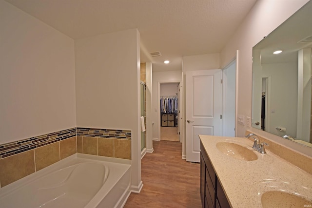 full bath with double vanity, a garden tub, a walk in closet, a shower stall, and a sink